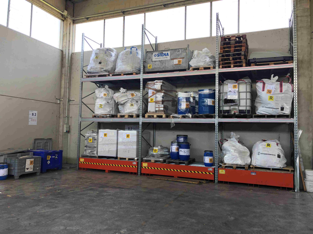 scaffalature con fusti e cisternette di rifiuti etichettati e stoccati in sicurezza.
